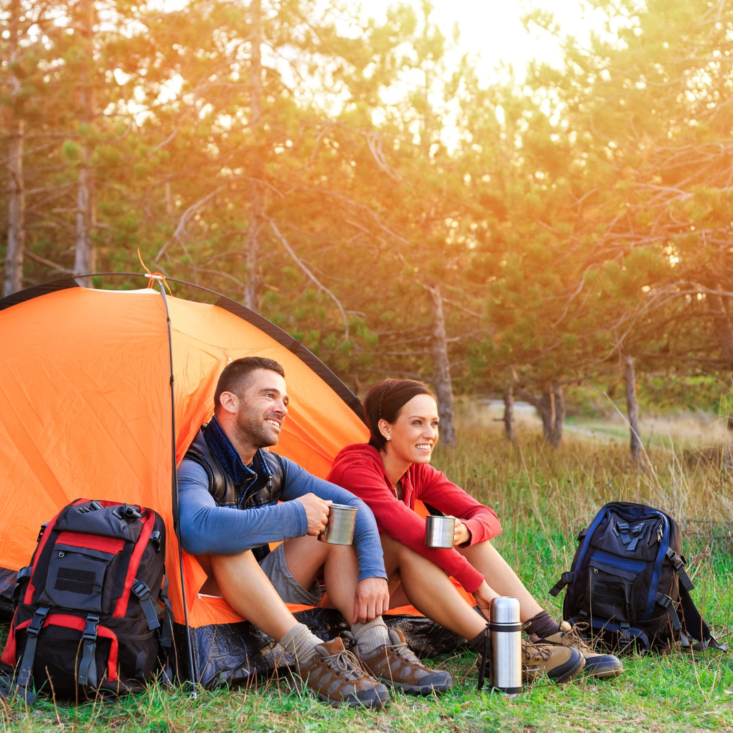 Two people sitting outside an orange tent in a forest during sunset.