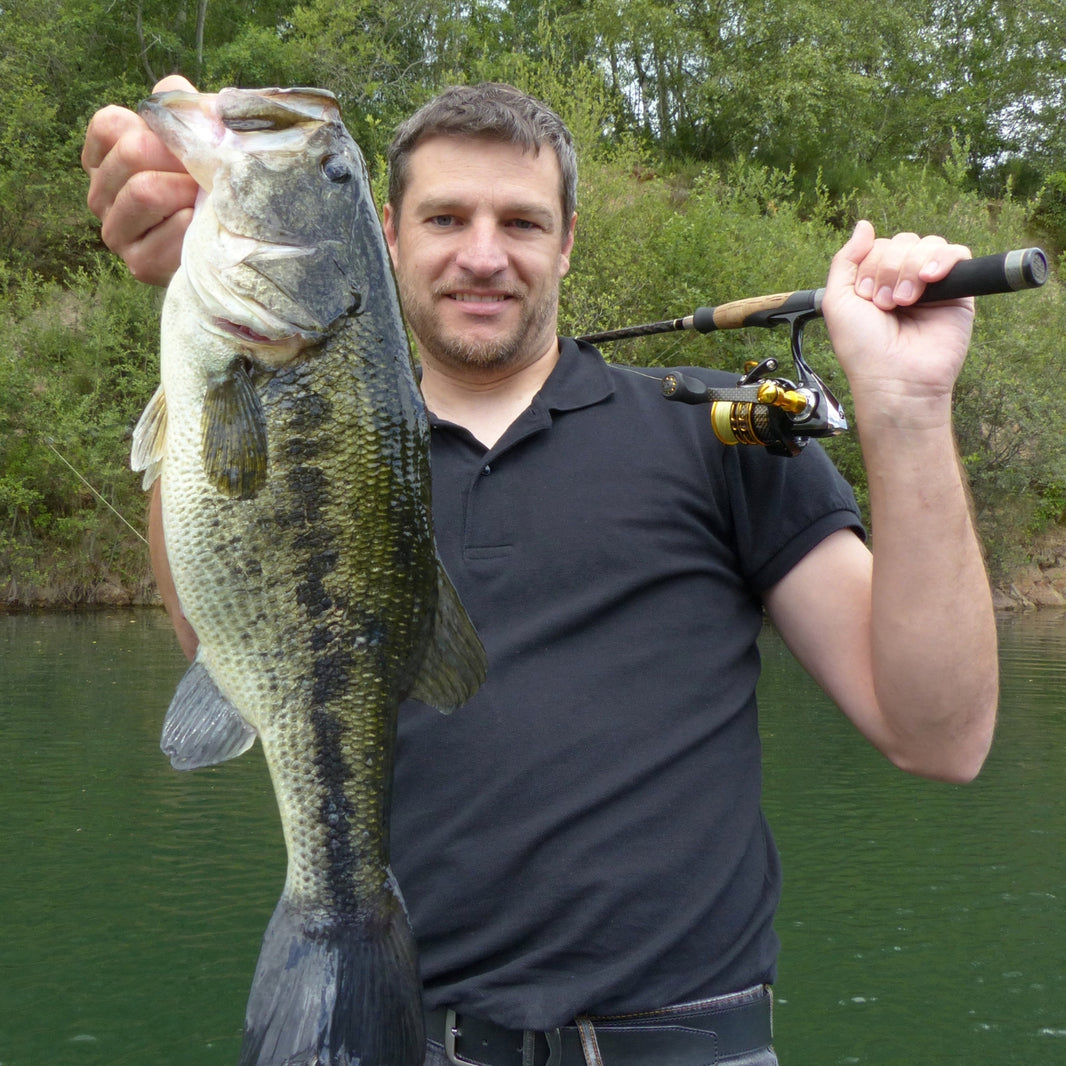 Man holding a large fish and a fishing rod by a body of water with trees in the background