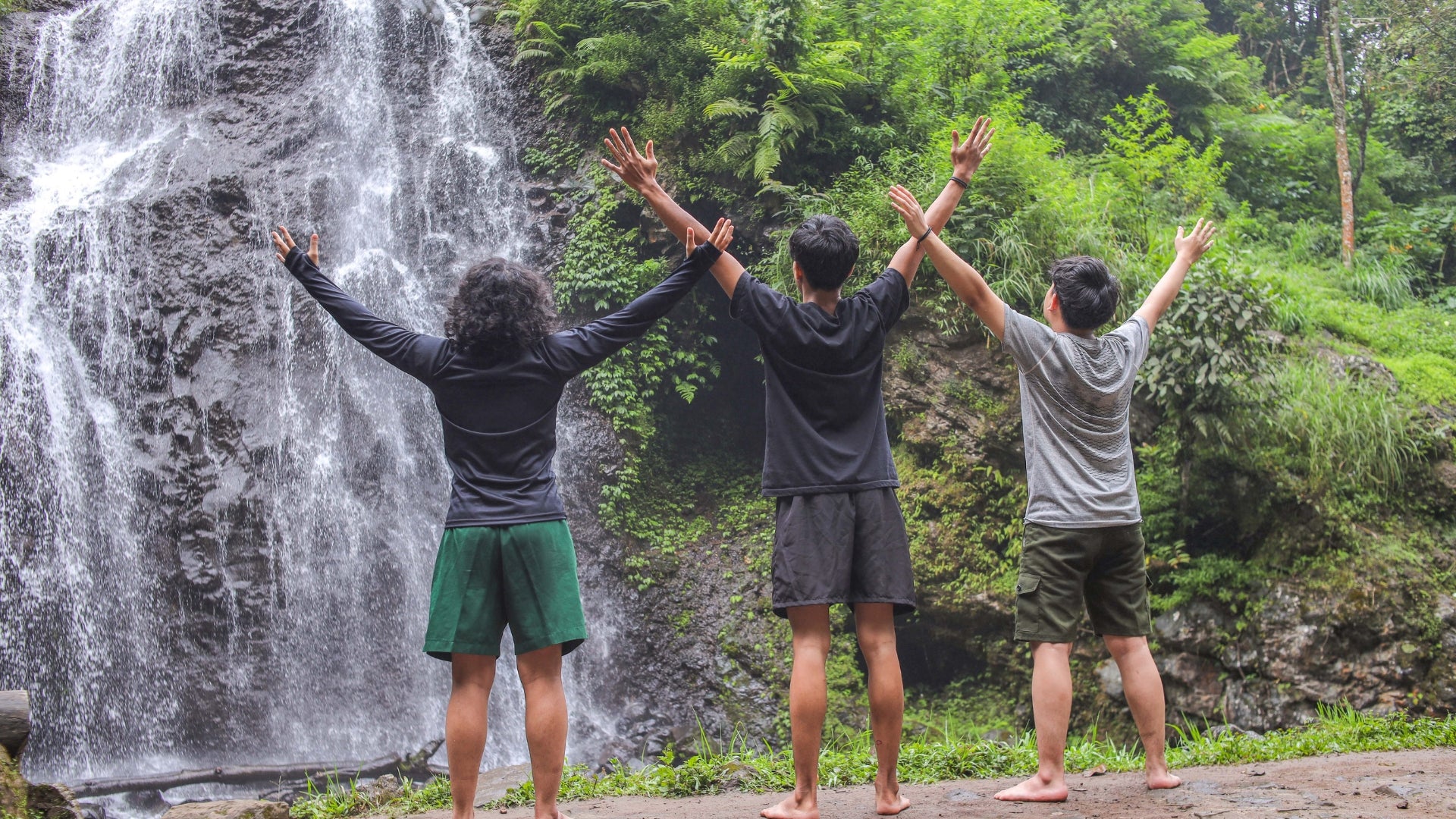 Three people with arms raised in front of a waterfall